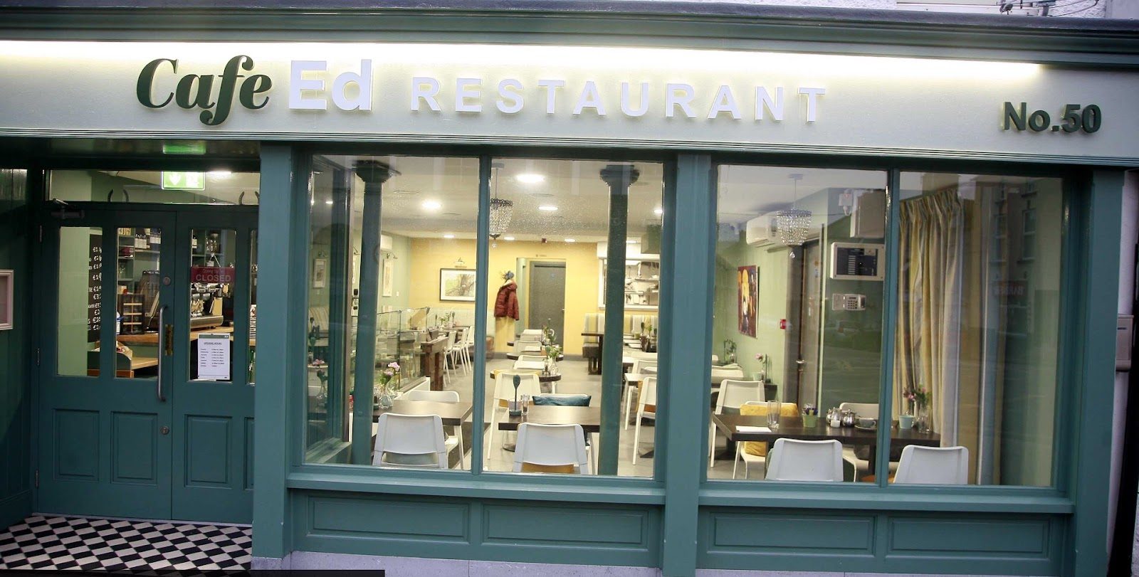 The green shopfront of Cafe Ed Restaurant, No. 50, lit in the evening, with the dining room visible through the windows.